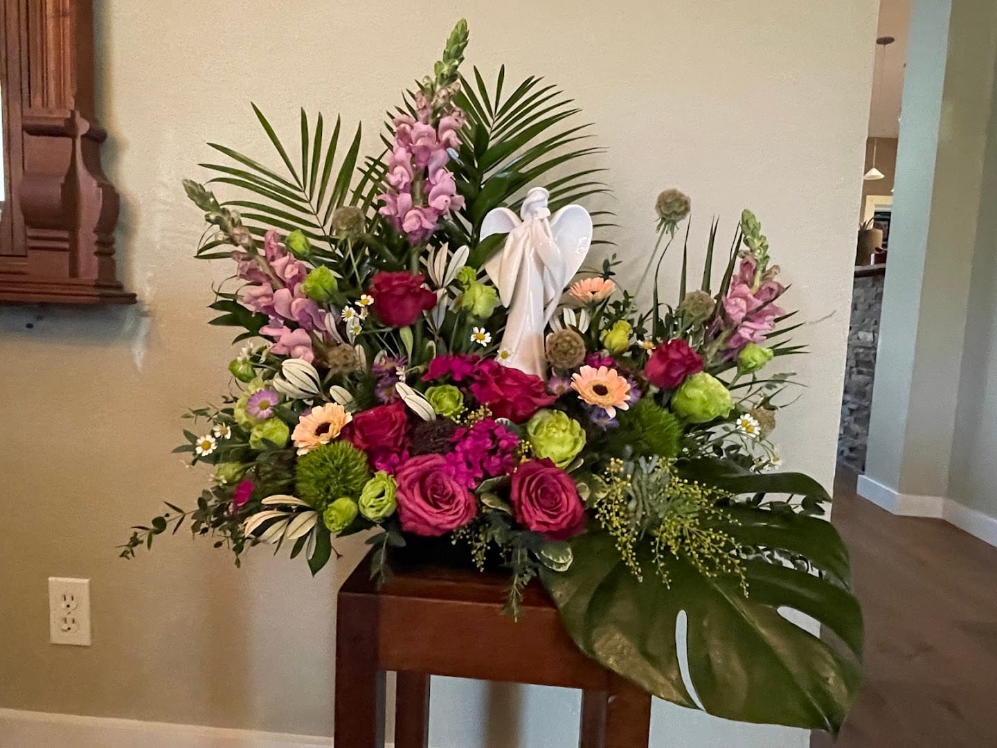 Large colorful floral arrangement surrounding a white ceramic angel figurine