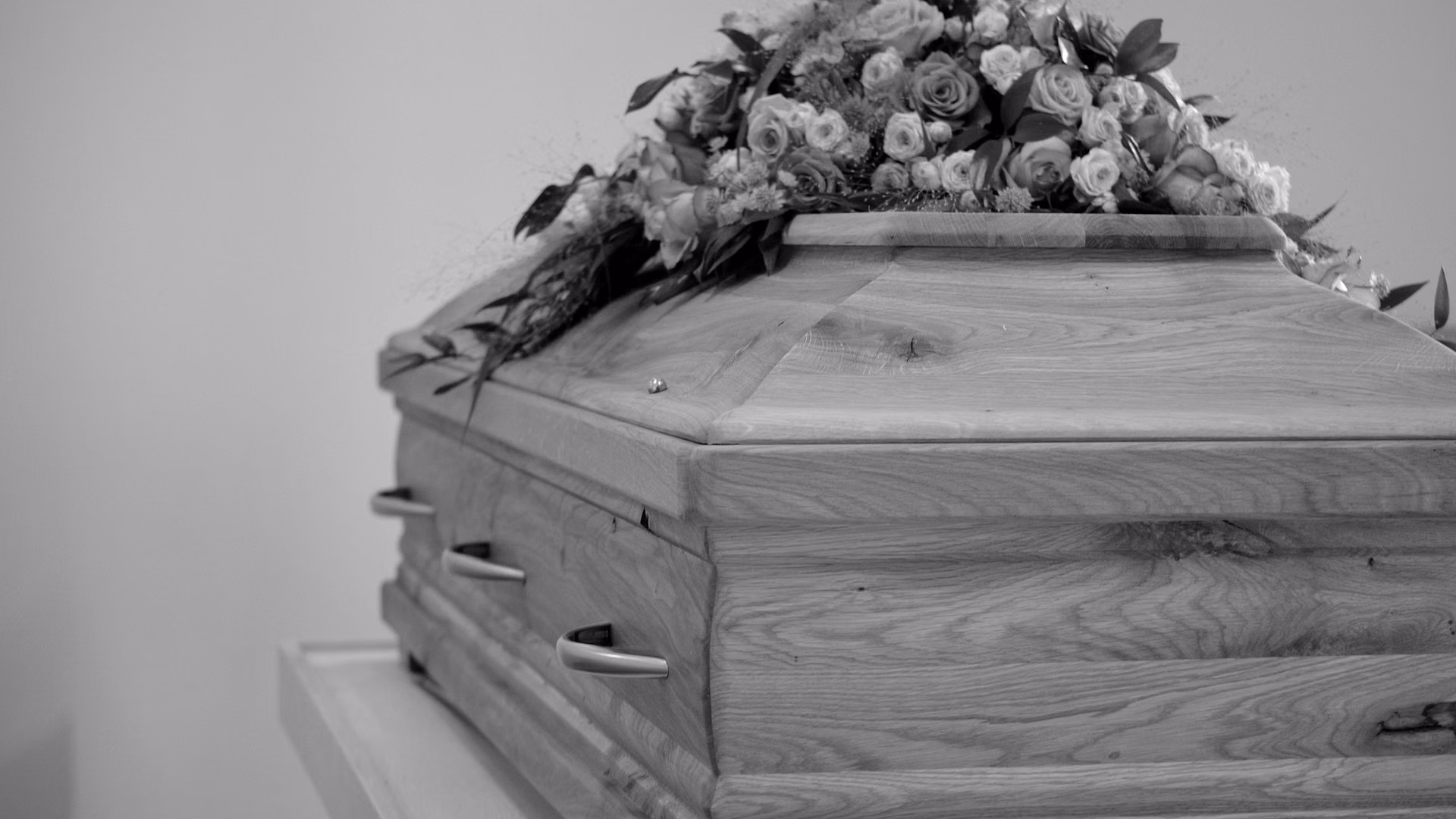 Black and white photo of a wooden coffin adorned with a detailed floral arrangement.