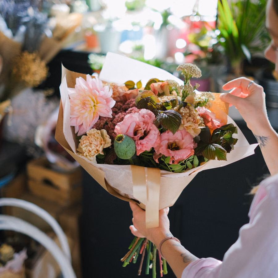 A woman holding a colorful flower bouquet in a cozy flower shop setting.