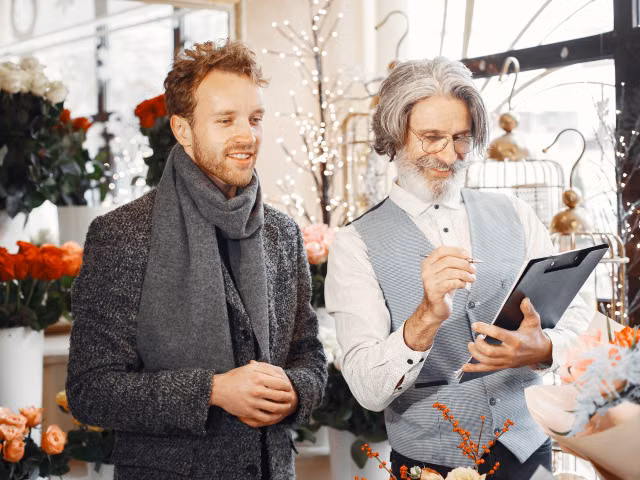 Two men conversing in a flower shop surrounded by vibrant bouquets and arrangements.