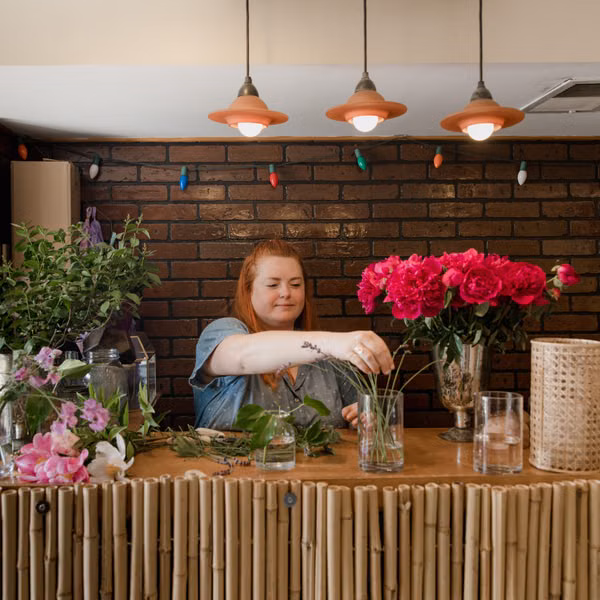 A female florist arranging a vibrant bouquet in an indoor floral shop setting.